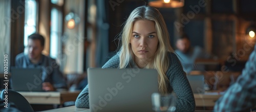 A woman is comfortably seated in a cafe, focused on her laptop screen while sipping a beverage