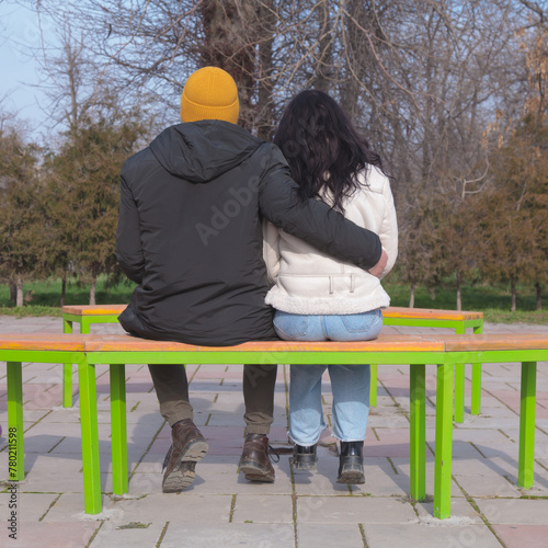 A couple in love hugs on a bench. Girl and guy in winter clothes sitting in the park, romantic date, happy lovers