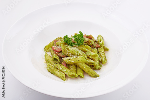 Penne pesto sauce with ham and bacon top with basil leaves served on white plate isolated on white background.