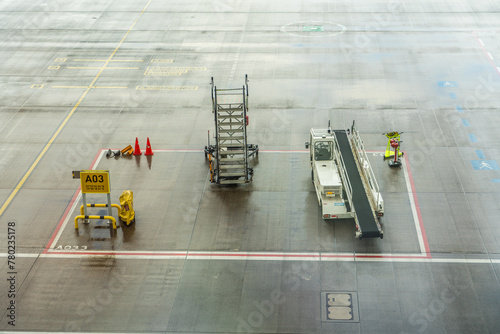 Airport Apron without Airplane but with Ground support equipment like passenger boarding stairs, belt loader, chocks and fire extinguisher  parked in a red marked square for the next use. 