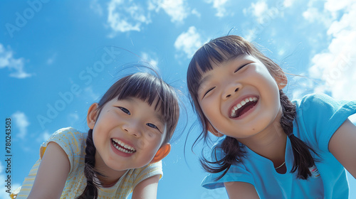 青空の下、遊ぶ笑顔な小学生の女の子2人がカメラを覗き込んでいるローアングル