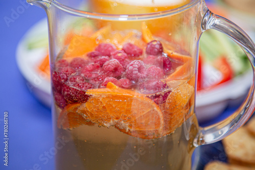 Decanter of chilled refreshing fruit drink with pieces of orange and berries. Close-up.