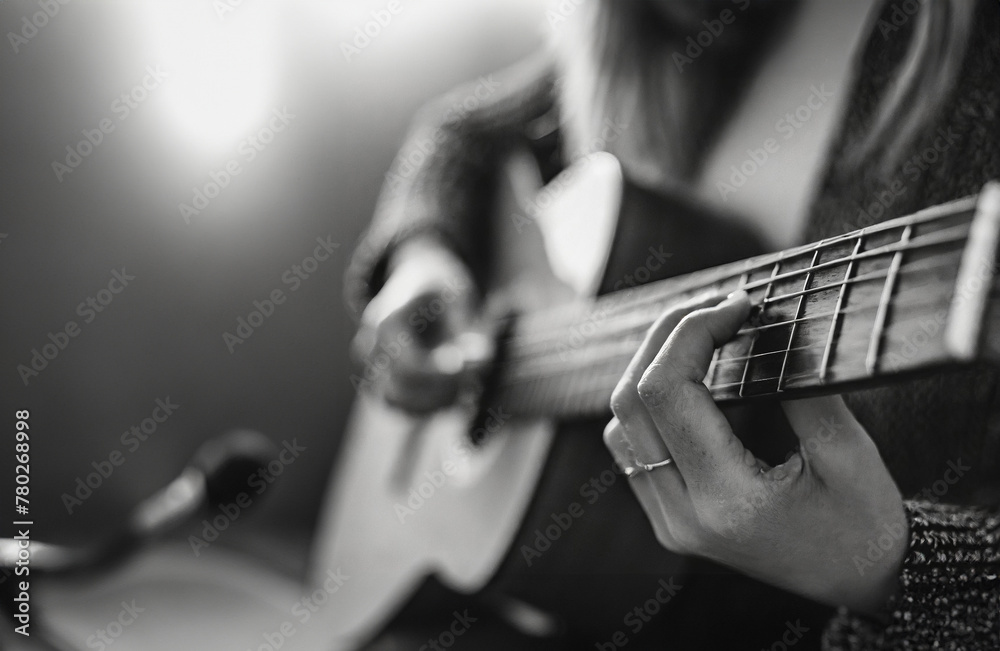 Fototapeta premium A female musician plays an acoustic guitar while recording at a studio into a microphone - the camera focuses on her fingers and the fretboard and the body of the guitar is in soft focus, live concert