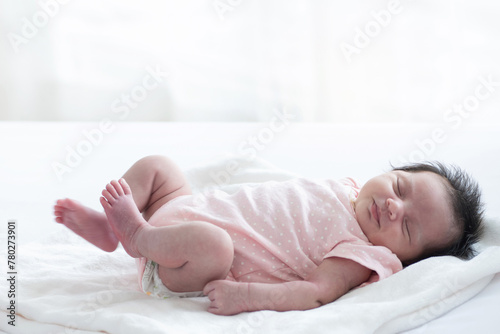 Newborn baby sleeping on white blanket in front of a window acts like she's startled from a bad dream