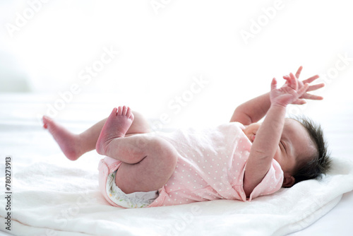 Newborn baby sleeping on white blanket in front of a window acts like she's startled from a bad dream