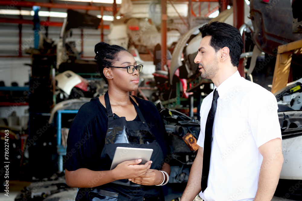 Happy harmony people at workplace, smiling white guy and African American woman working together Two workers check stock at auto spare parts store shop warehouse, surrounded by secondhand engine parts