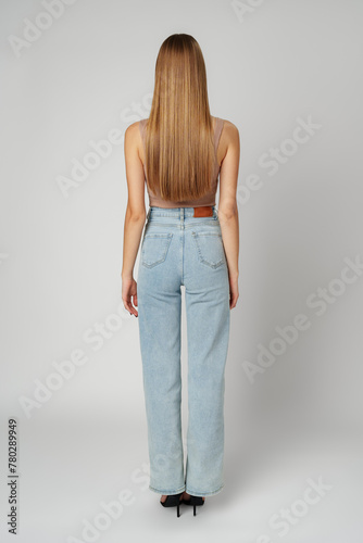 Back view full length photo of young woman with long hair on gray background