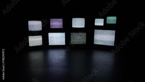 A wall of assorted old cathode televisions in a dark and isolated room.
