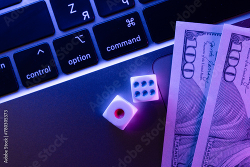 Close-up view of modern laptop keyboard with dices and dollar bills fragments scattered on the keys, symbolizing the concept of online casino and dice games on a digital platform.