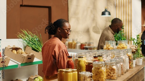 African american client examines bio homemade bulk products, looking to buy natural ethically sourced food alternatives for healthy nutrition. Woman shopping for goods at zero waste store. Camera 1.