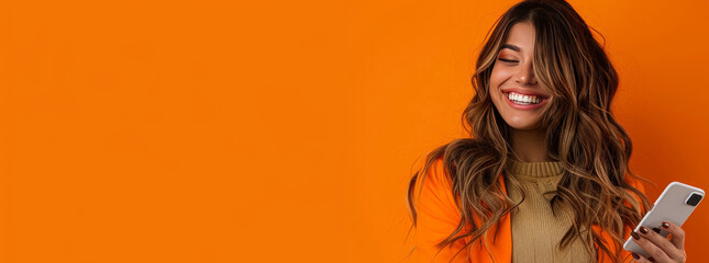 Photo of An elegant young woman in her 20s with long wavy hair, happy smiling while using an mobile phone on a orange and black background with copy space for text or product. Web banner.