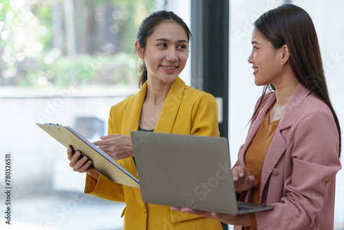Two pretty young Asian businesswomen standing to discuss working on investment projects and planning strategies together at the office. brainstorming concept.