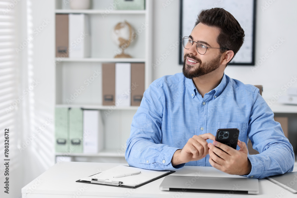 Happy young man using smartphone at white table in office, space for text Happy young man using smartphone at white table in office, space for text