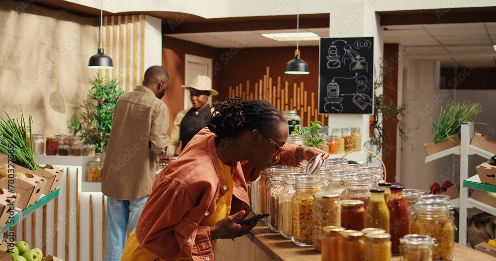 Customer checking shopping list on phone before choosing products, trying to buy organic locally grown food for low carbon footprint. African american woman looking at checklist notes. Camera 2. Customer checking shopping list on phone before choosing products, trying to buy organic locally grown food for low carbon footprint. African american woman looking at checklist notes. Camera 2.