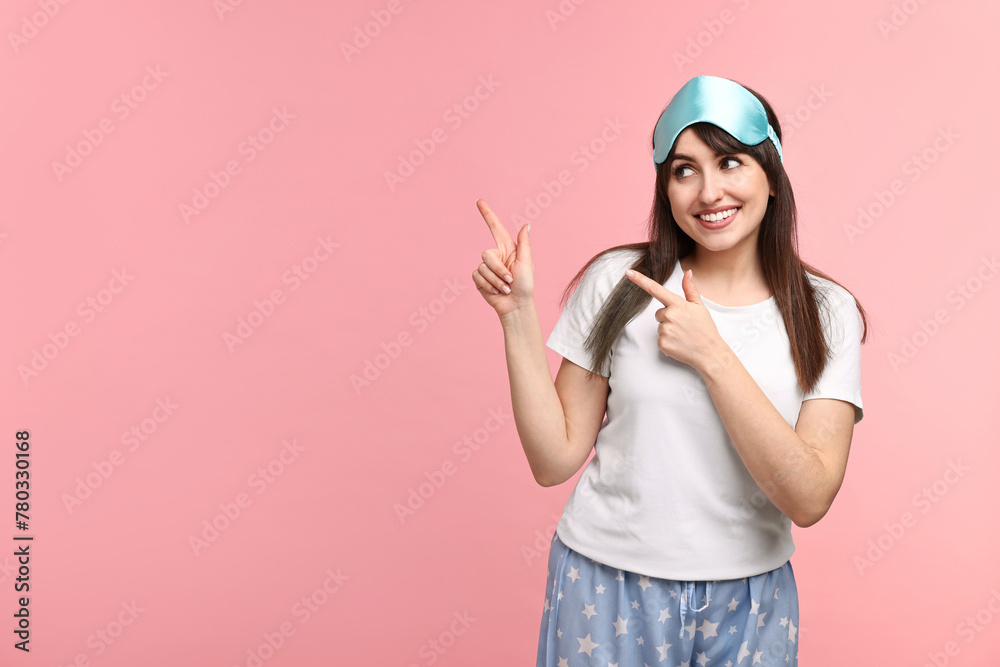 Happy woman in pyjama and sleep mask pointing at something on pink background, space for text Happy woman in pyjama and sleep mask pointing at something on pink background, space for text