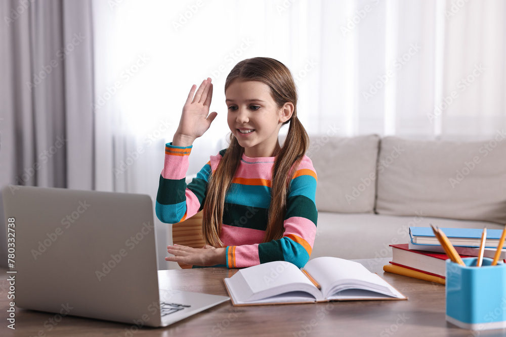 E-learning. Cute girl raising her hand to answer during online lesson at table indoors E-learning. Cute girl raising her hand to answer during online lesson at table indoors