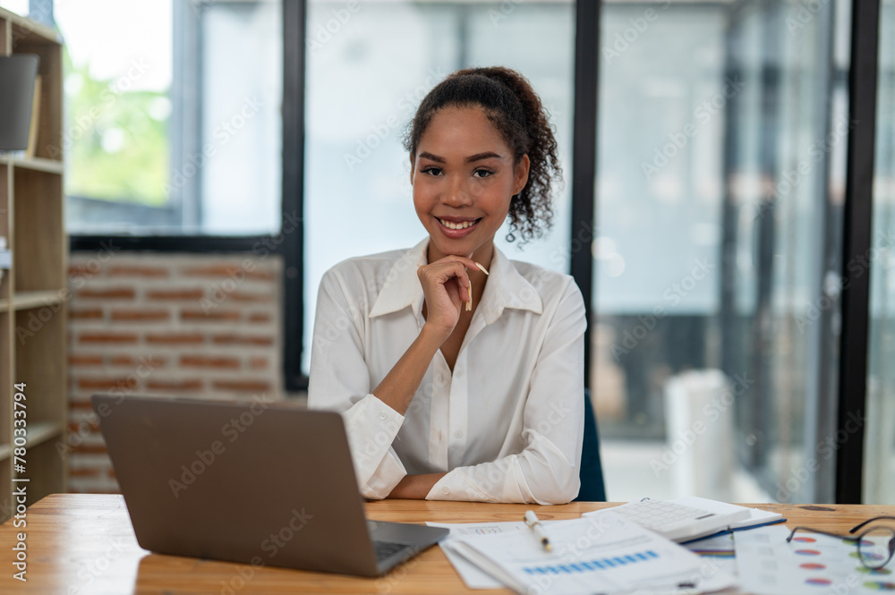 A young, cheerful professional woman sitting at her desk in a bright office environment, looking confidently at the camera. A young, cheerful professional woman sitting at her desk in a bright office environment, looking confidently at the camera.