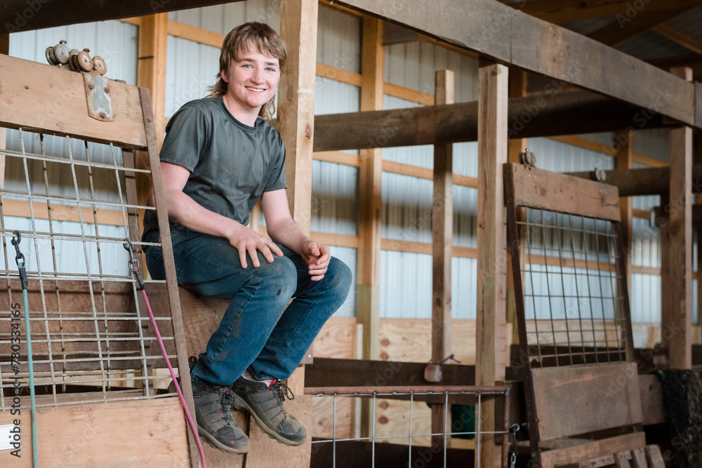 Smiling teen farm boy sitting on rail in barn. Smiling teen farm boy sitting on rail in barn.