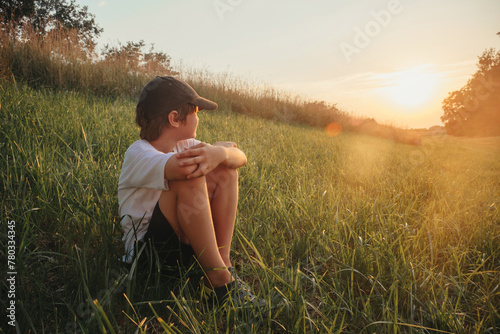 Happy boy sitting on grass field wearing white t-shirt, sunset