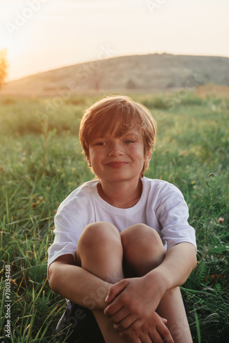 Happy boy sitting on grass field wearing white t-shirt
