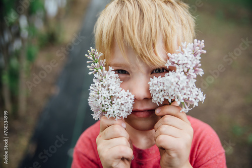 Portrait of boy holding lilac flowers up to face outdoors in summer photo