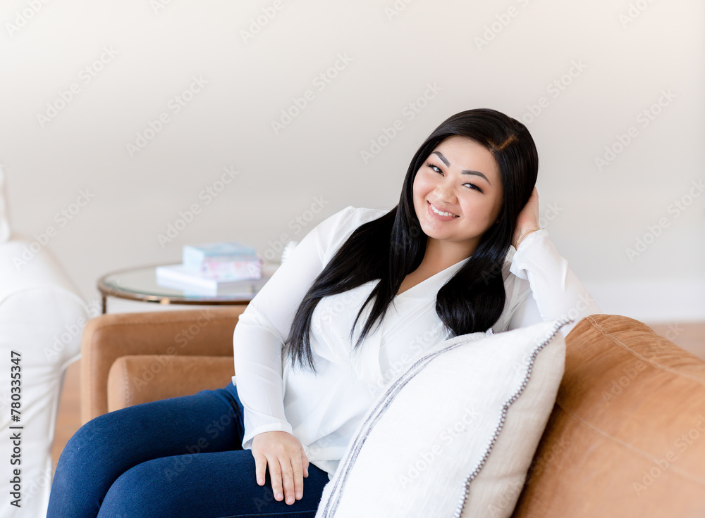 Asian woman sitting on brown leather couch smiling Asian woman sitting on brown leather couch smiling