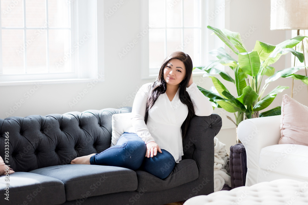 Young asian woman smiling and sitting on couch in a bright airy Young asian woman smiling and sitting on couch in a bright airy