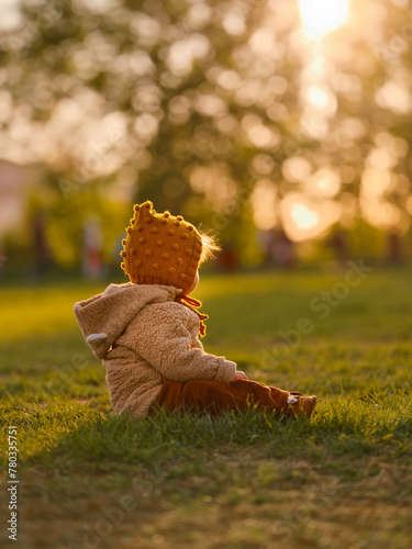 A three-year-old girl is sitting on the grass in the central park.