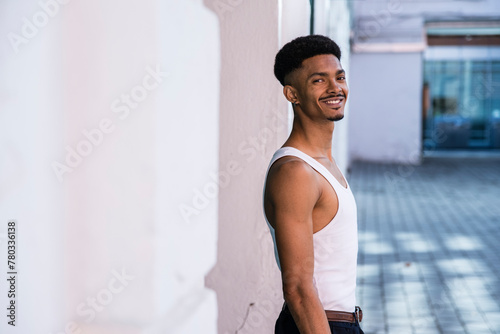 Handsome smiling man posing sideways outside next to a white wall. photo