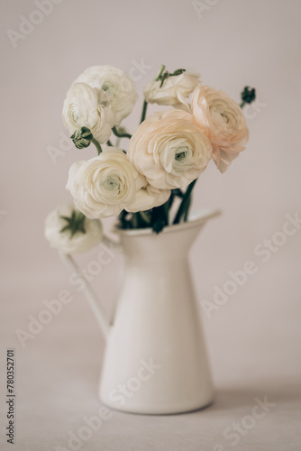 Cream buttercups (Ranunculus) in a white vase on a light background. 