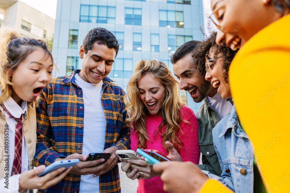 © Xavier Lorenzo - Group of young people using mobile phone together at city street. Millennial student friends enjoying social media content or playing video games on cellphone app at college campus