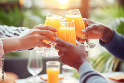 Multiethnic Hands Toasting with Orange Juice Glasses Over the Tabletop at Social Gathering