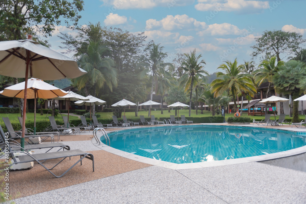 Beautiful swimming pool in tropical resort with palms chairs loungers under umbrella . Luxury travel vacation