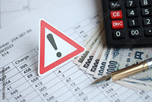 Exclamation sign and japanese tax calculations lies on table with calculator, pen and japanese yen money bills close up photo