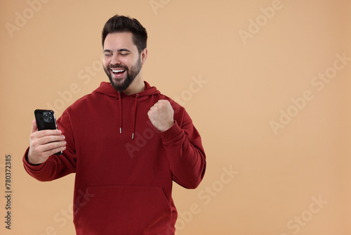 Happy young man using smartphone on beige background, space for text