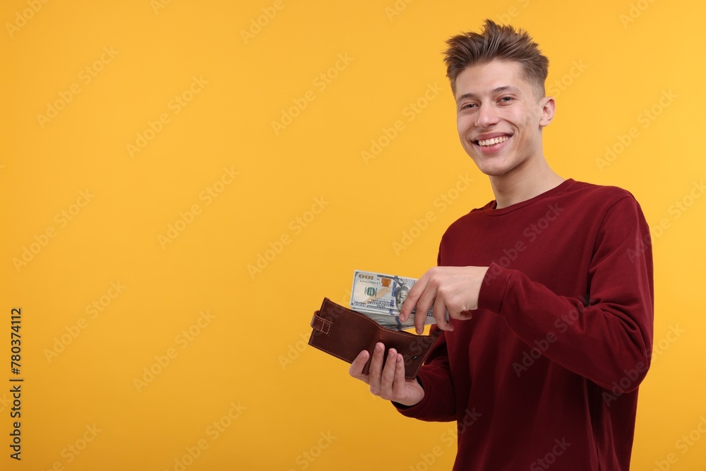 Happy man putting money into wallet on yellow background. Space for text Happy man putting money into wallet on yellow background. Space for text