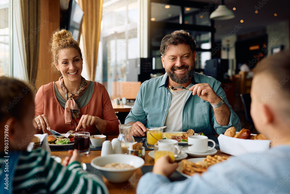 Happy parents talking to their kids while eating breakfast in  hotel.