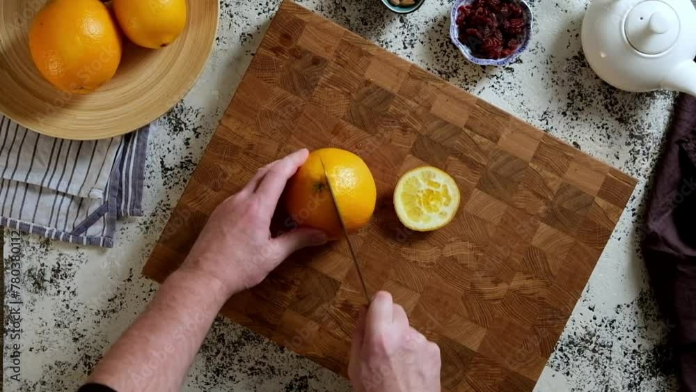 Top view of a man cutting large oranges on a wooden cutting board.