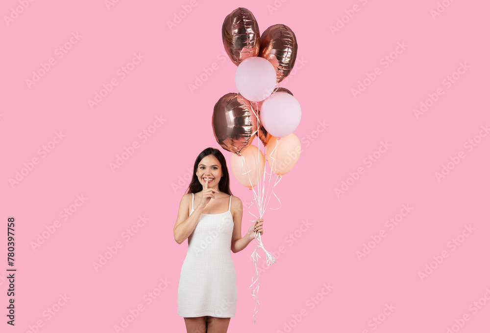 Smiling woman holding festive balloons on pink background