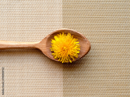 household item, wooden kitchen spoon with one yellow dandelion on yellow and white striped tablecloth, place for text and logo	
