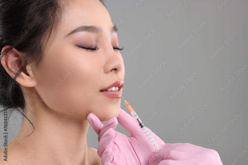Woman getting lip injection on grey background