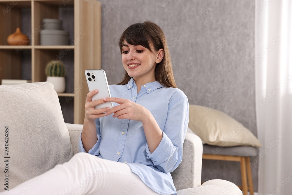 Beautiful young housewife using smartphone on sofa at home Beautiful young housewife using smartphone on sofa at home