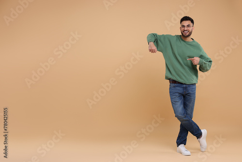 Happy young man pointing at something on beige background, space for text