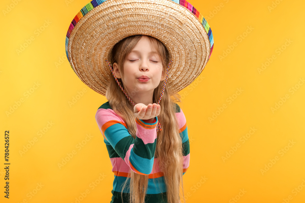 Cute girl in Mexican sombrero hat blowing kiss on orange background Cute girl in Mexican sombrero hat blowing kiss on orange background