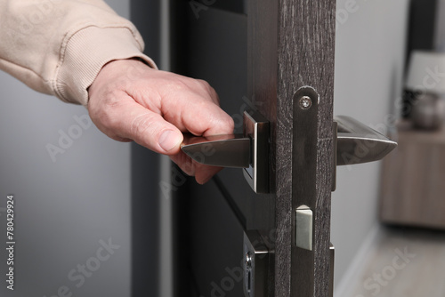 Man opening wooden door indoors, closeup of hand on handle photo