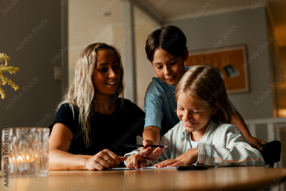 Woman with smiling sons doing homework together at home Woman with smiling sons doing homework together at home