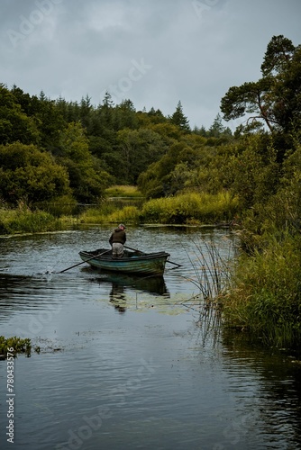 Vertical shot of a man in the small boat in a lake surrounded by a forest on a gloomy day © Wirestock