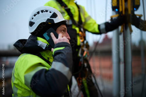 Male rope access worker talking on phone outside window of building photo