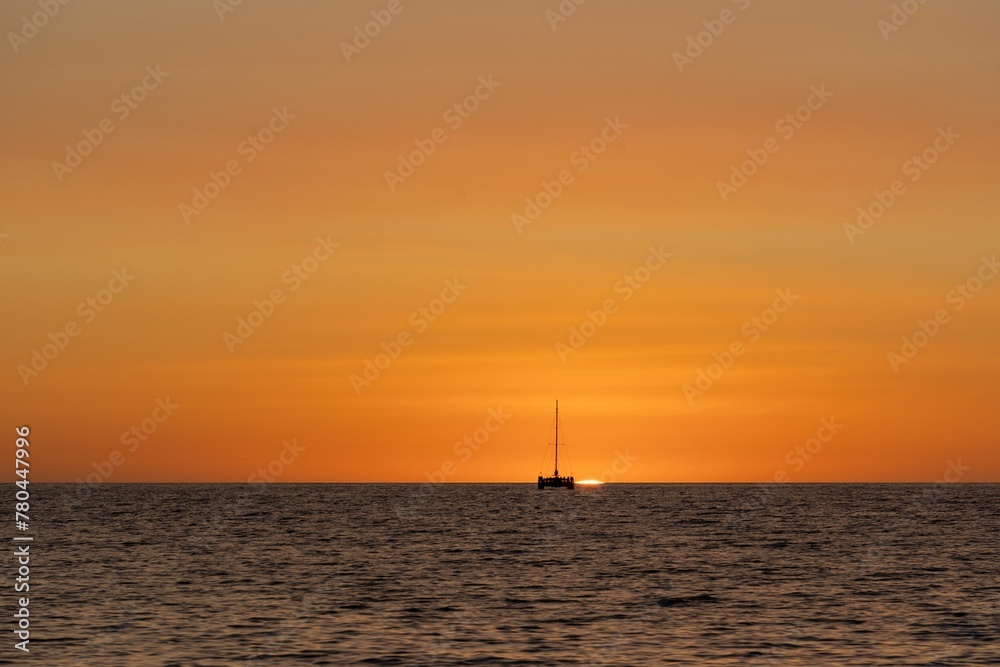 Silhouette of a sailboat in the distance on the water at sunset