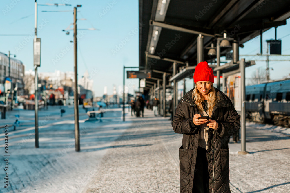 Woman text messaging on mobile phone while standing at bus stop Woman text messaging on mobile phone while standing at bus stop